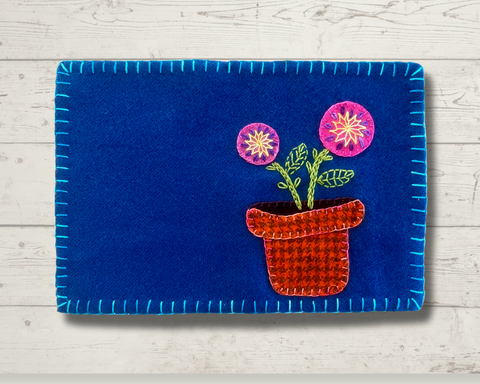 Photo of a blue wool mug rug with a potted plant embellished with wool thread and perle cotton embroidery.