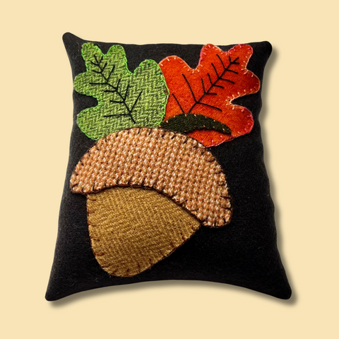 Photo of a pincushion with a wool appliqué acorn and green and red leaves