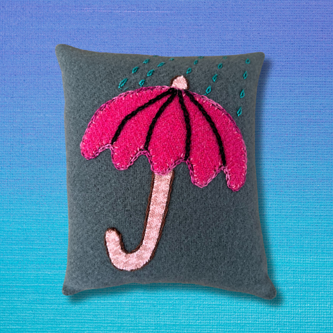 Photo of a wool appliqué pincushion with an umbrella and embroidered raindrops.