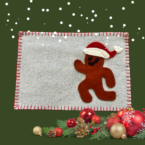 Photo of a wool appliqué mug rug with a gingerbread person in a santa hat.