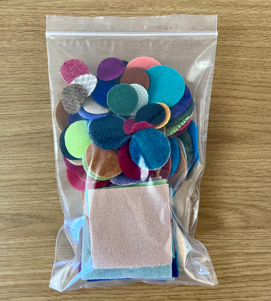 A photo of a plastic bag that contains wool squares and die cut circles for wool appliqué embroidery.