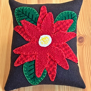 Photo of a wool appliqué pincushion with a wool appliqué poinsettia and embroidery stitches.