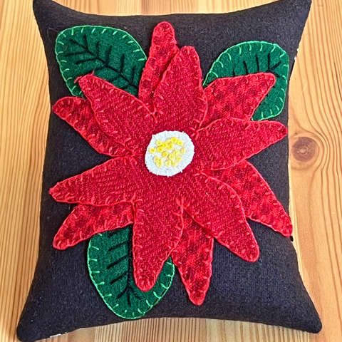 Photo of a wool appliqué pincushion a wool poinsettia and hand embroidery stitches.