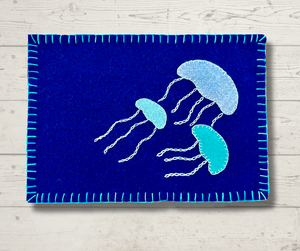 Photo of a wool appliqué mug rug with three wool jellyfish embellished with perle cotton embroidery.
