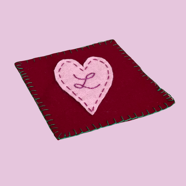 red wool coaster with a pink heart and the letter L embroidered on the front