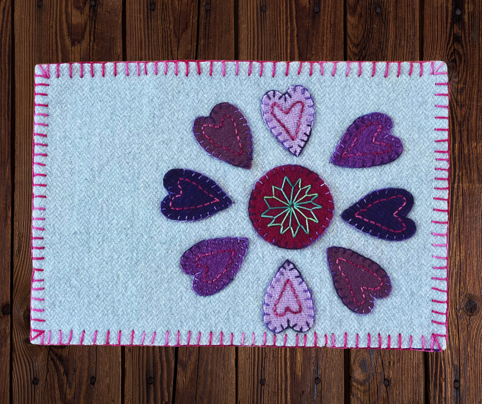 Photo of a wool appliqué mug rug with a heart petals and circle center with perle cotton embroidery.