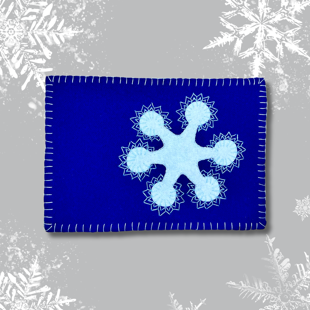 Photo of a blue wool mug rug with a white wool snowflake with embroidery.