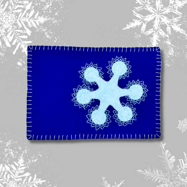 Photo of a blue mug rug with a white embroidered snowflake wool appliqué kit.