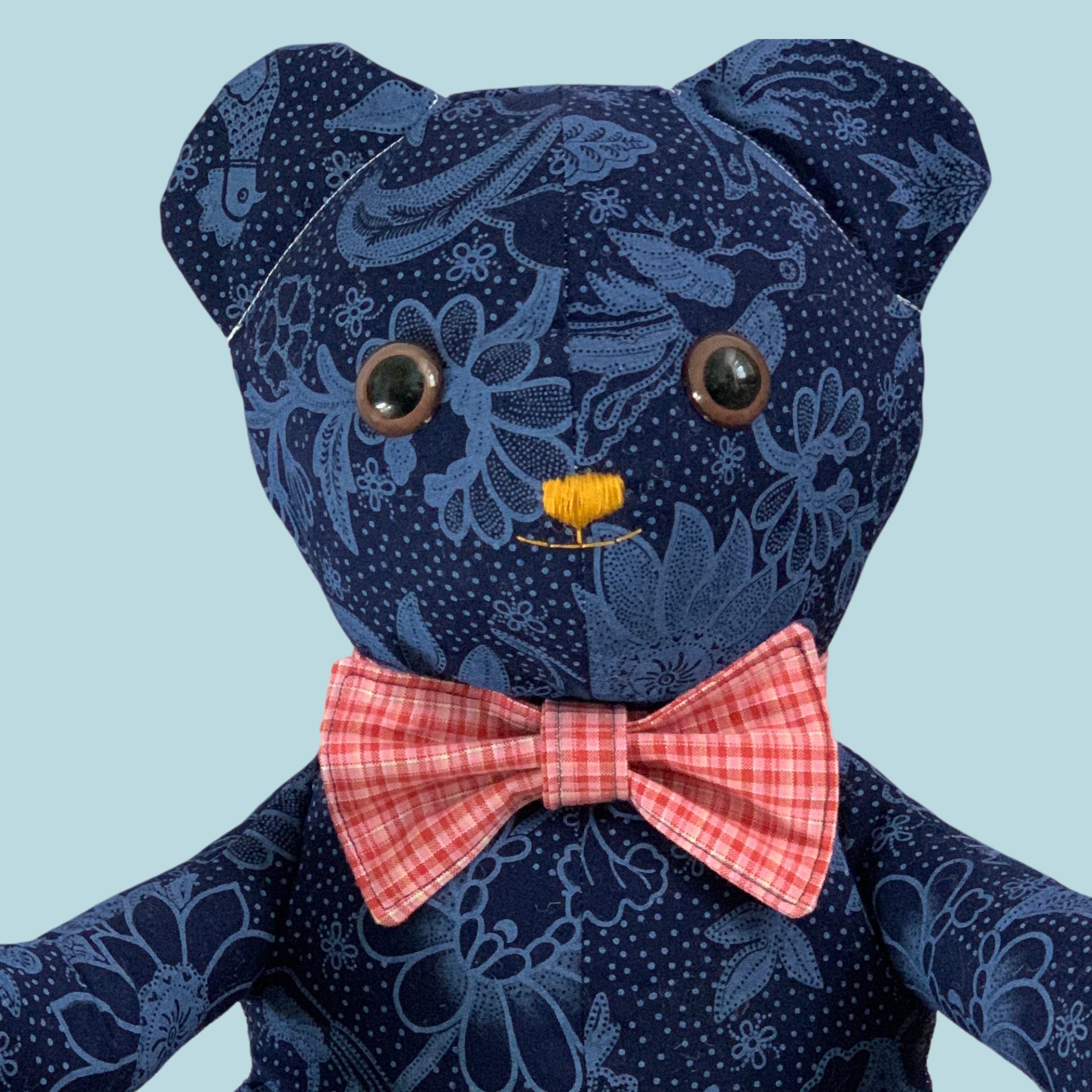 photo of a blue stuffed bear wearing a red plaid bow-tie