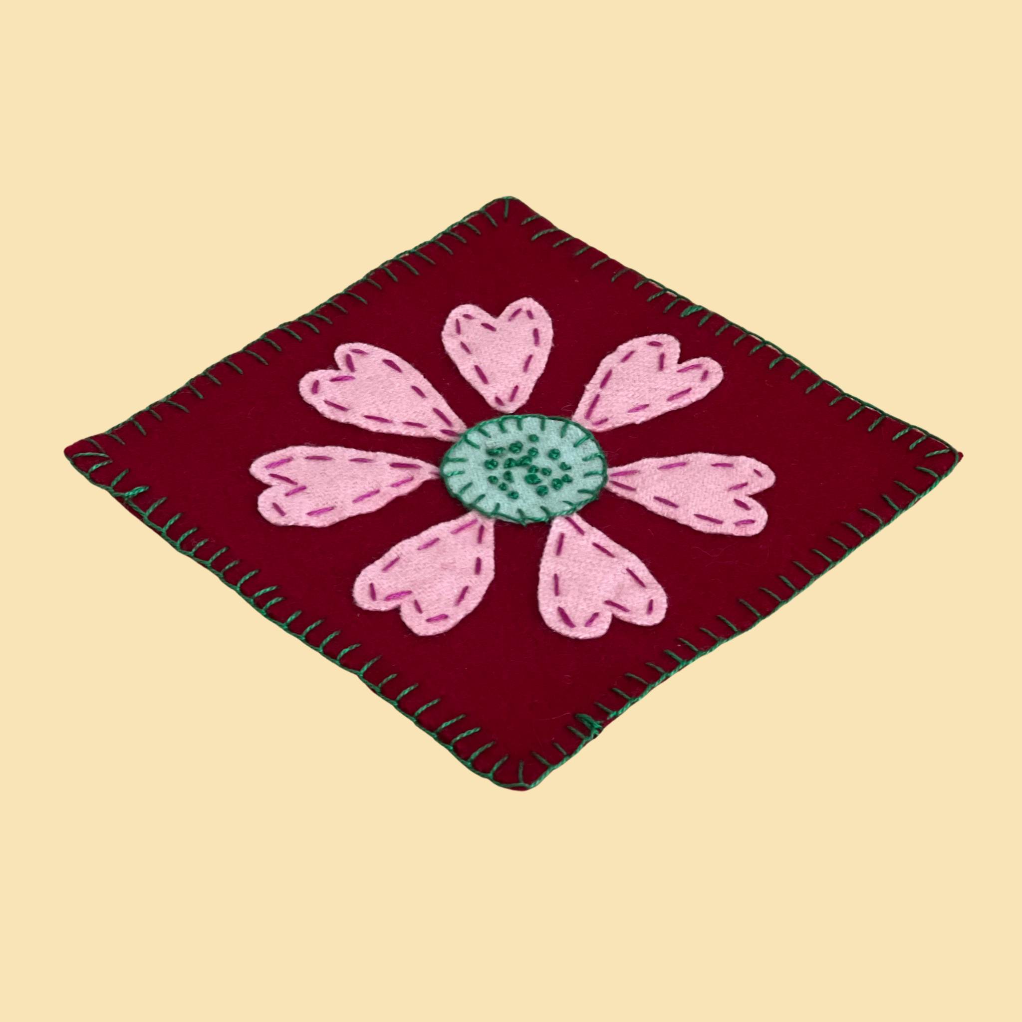 photo of a wool applique coaster with heart petals and french knots